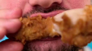 Tıraşsız beyaz adam tavuk etiyle kemik kemiriyor. Hızlı restoranda sağlıksız yemekler yiyor. Fast food yiyen yakın plan adam, lezzetli altın çıtır tavuk gevrek ekmekli koca bacak..