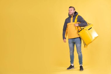 Yemek teslimatı. Sarı ceketli ve sarı arka planda termos çantalı beyaz adam gülümsüyor. Şehre ekspres yiyecek teslimatı kavramı, metin ve slogan için yeri olan pankart.
