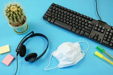 Bitki, klavye, kalem, tıbbi maske, kulaklık. Salgın zamanda işyeri. Coronavirus COVID-19 konsepti. Üst görünüm