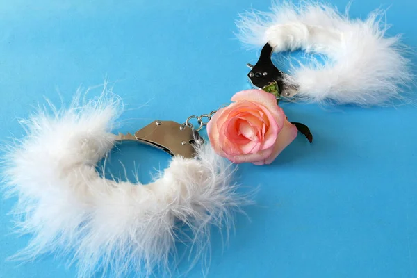 Mavi arka planda gül çiçekleri olan beyaz tüylü kelepçeler, nazik seks oyunları konsepti