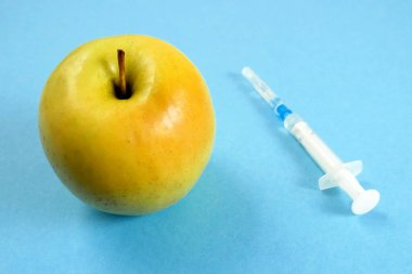Elma, genetik mühendisliği laboratuvarında mavi arka planda şırınga ve test tüpleriyle, GMO gıda kavramı