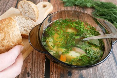 Tabakta sebze çorbası, yeşillikler ve ahşap masada ekmek.