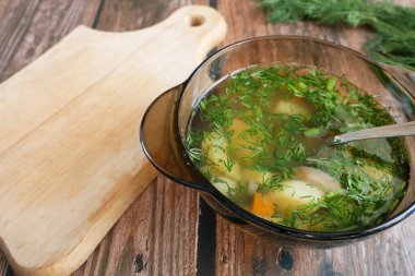 Tabakta sebze çorbası, yeşillikler ve ahşap masada ekmek.