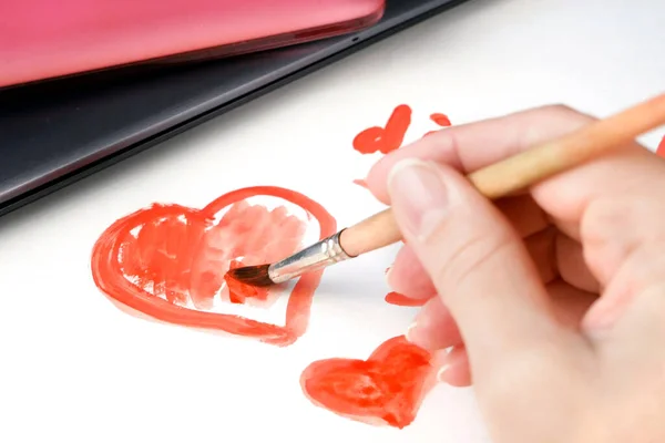 digital detoxing concept, person draws heart by paints on paper sheet on laptop and phone background