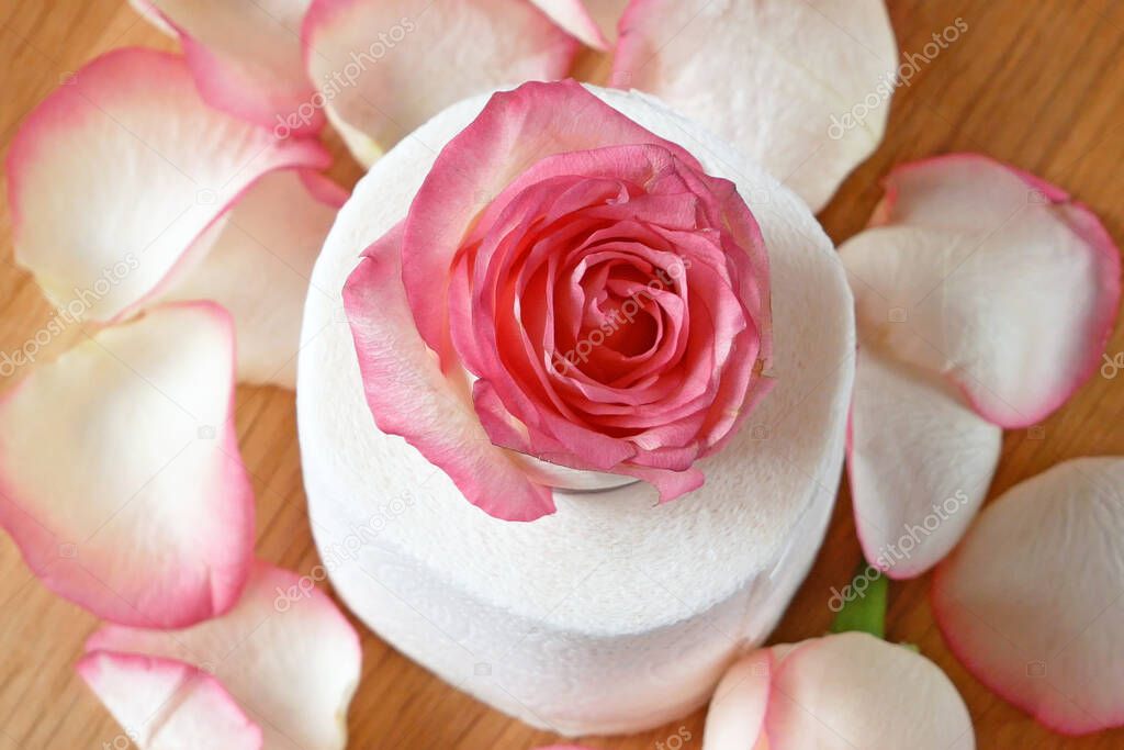 roll of toilet paper with fresh roses and petals rotates on wooden background, gentle and soft toilet paper with rose fragrance concept