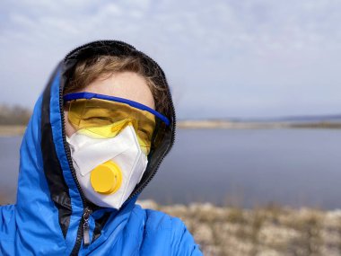 Koruyucu maskeli ve gözlüklü bir kadın ve evin arka planında bir kaput, koronavirüs konsepti, çevre felaketi konsepti