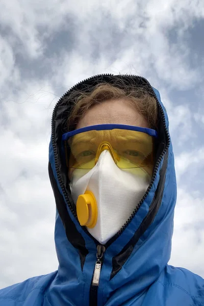 woman in a protective mask and glasses and a hood outdoors on  ruined house background, coronavirus concept, concept of environmental disaster