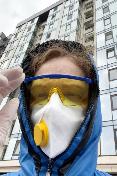 woman in a protective mask and glasses and a hood outdoors on  ruined house background, coronavirus concept, concept of environmental disaster