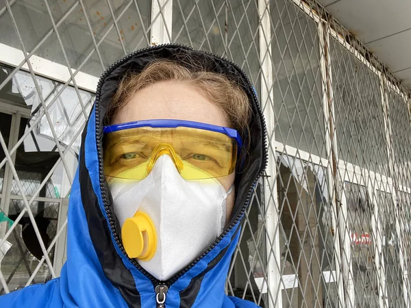 woman in a protective mask and glasses and a hood outdoors on  ruined house background, coronavirus concept, concept of environmental disaster