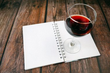 Bir kadeh kırmızı şarap ve koyu ahşap arka planda boş not defteri. Kopyalama alanı olan üst görünüm