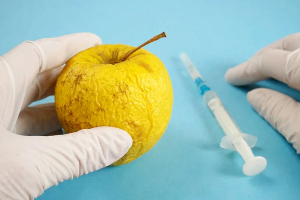 apple in genetic engineering laboratory with syringe and test tubes on blue background, gmo food concept