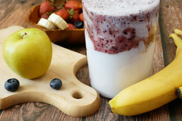 Making Fruit Smoothie with banana, blueberry, strawberry and milk. Blender filled with fresh whole fruits for making a smoothie or juice