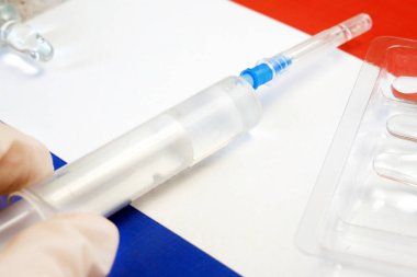 Aşılı şırınga, Fransız bayrağının arka planında, Coronavirus aşısına karşı bir eldivenin içinde elle tutulur.