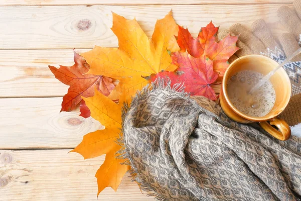 Sonbahar yaprakları, sabah kahvesi ve ahşap arka planda sıcak bir eşarp, sonbahar havası konsepti.