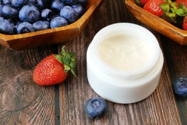 Doğal krem kozmetik kavanozda taze çilek ve yabanmersini arkaplanda