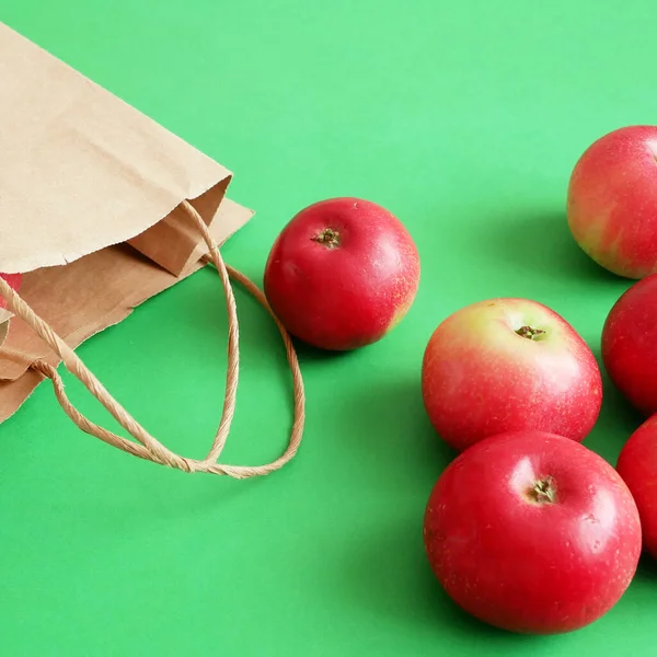 many red apples and paper bag on green background, green grocery