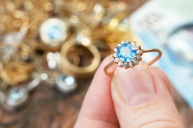 Eline büyük bir topaz taşı, bir sürü elmas, altın, gümüş ve para mücevheri, rehinci konsepti, yakın plan...