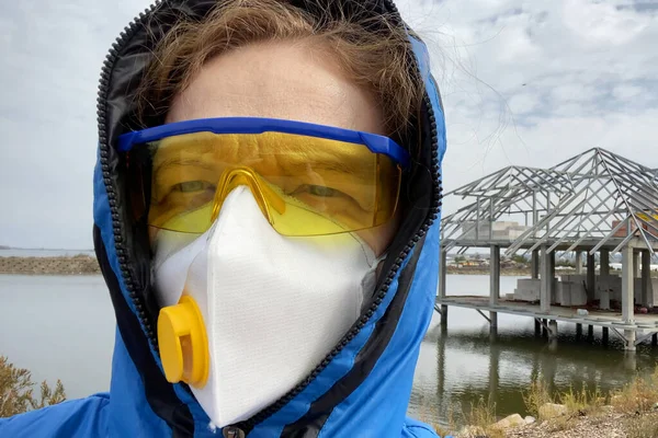 woman in a protective mask and glasses and a hood outdoors, coronavirus concept, concept of environmental disaster, closeup