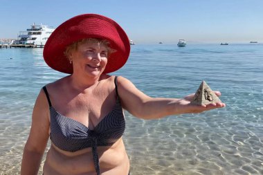 Woman in swimsuit holding souvenirs of the pyramids in her hand on the sed background, tourism in Egypt concept, travel and vacation, outdoors