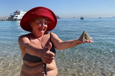 Woman in swimsuit holding souvenirs of the pyramids in her hand on the sed background, tourism in Egypt concept, travel and vacation, outdoors