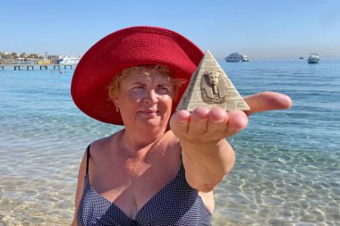 Woman in swimsuit holding souvenirs of the pyramids in her hand on the sed background, tourism in Egypt concept, travel and vacation, outdoors