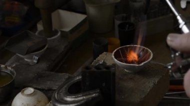 Kuyumcu bir potada sıvı halde altını eritir. Makro video. Profesyonel aletlerle mücevher yapımı. El yapımı mücevherler, mücevher yapma süreci. Metal erimesi
