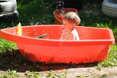 küçük bir çocuk sokakta küçük bir havuzda yüzüyor