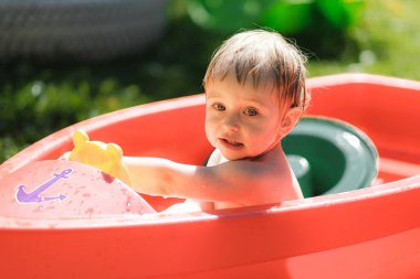 küçük bir çocuk sokakta küçük bir havuzda yüzüyor