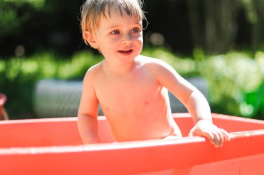 küçük bir çocuk sokakta küçük bir havuzda yüzüyor