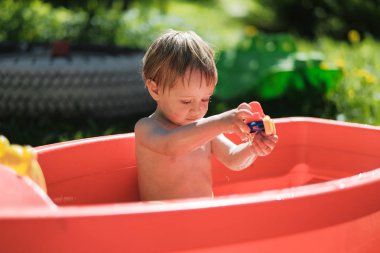 küçük bir çocuk sokakta küçük bir havuzda yüzüyor