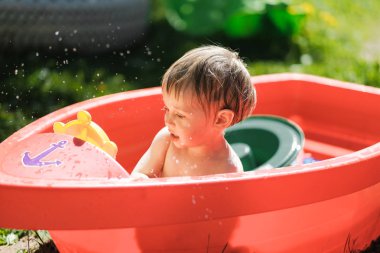 küçük bir çocuk sokakta küçük bir havuzda yüzüyor
