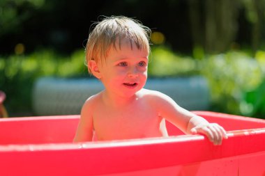 küçük bir çocuk sokakta küçük bir havuzda yüzüyor