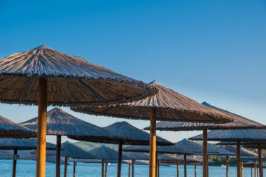 Arka planda turkuaz su ile plajda şemsiye saman kaplı