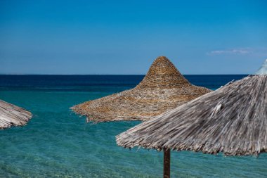 Arka planda turkuaz su ile plajda şemsiye saman kaplı