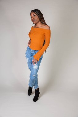 Genç bir siyah kadın beyaz bir arka plan üzerinde poz vintage turuncu üst ve bol kot ile stüdyo çekim