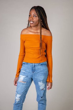 Genç bir siyah kadın beyaz bir arka plan üzerinde poz vintage turuncu üst ve bol kot ile stüdyo çekim