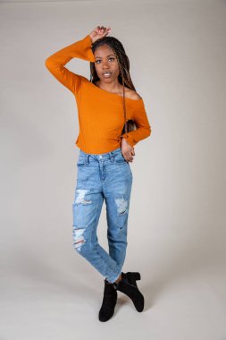 Genç bir siyah kadın beyaz bir arka plan üzerinde poz vintage turuncu üst ve bol kot ile stüdyo çekim
