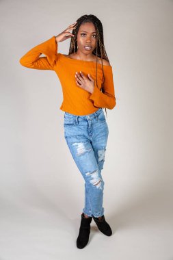 Genç bir siyah kadın beyaz bir arka plan üzerinde poz vintage turuncu üst ve bol kot ile stüdyo çekim