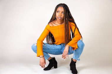 Studio bir beyaz arka plan çömelme poz vintage turuncu üst ve bol kot ile genç bir siyah kadın vurdu