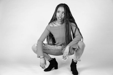 Studio bir beyaz arka plan çömelme poz vintage turuncu üst ve bol kot ile genç bir siyah kadın vurdu