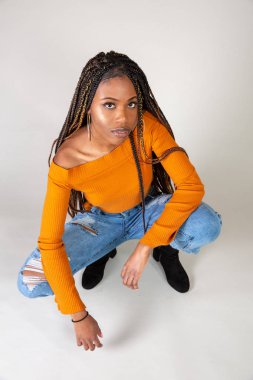 Studio bir beyaz arka plan çömelme poz vintage turuncu üst ve bol kot ile genç bir siyah kadın vurdu