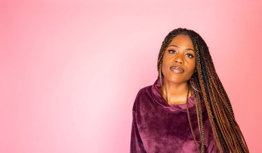 Bir rahat kentsel yaşam tarzı kıyafet pembe bir zemin üzerinde şaşırtıcı örgülü uzun saçlı Afrika kökenli Amerikalı kadın