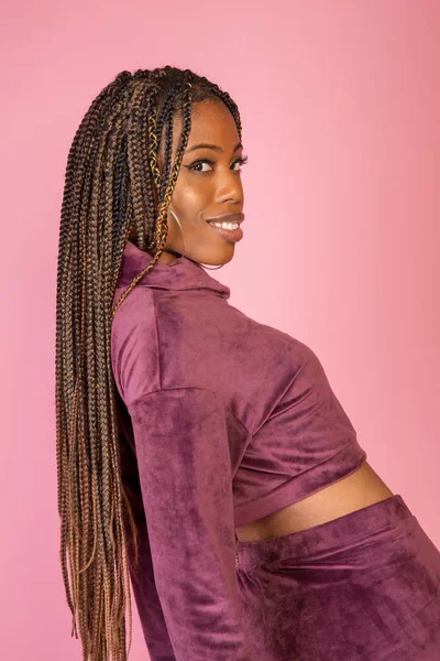 Bir rahat kentsel yaşam tarzı kıyafet pembe bir zemin üzerinde şaşırtıcı örgülü uzun saçlı Afrika kökenli Amerikalı kadın