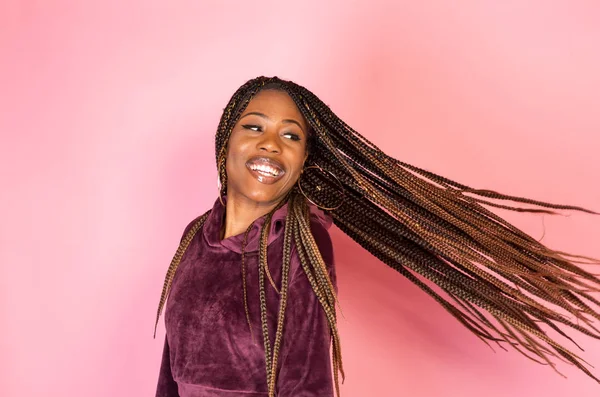 Bir rahat kentsel yaşam tarzı kıyafet pembe bir zemin üzerinde şaşırtıcı örgülü uzun saçlı Afrika kökenli Amerikalı kadın
