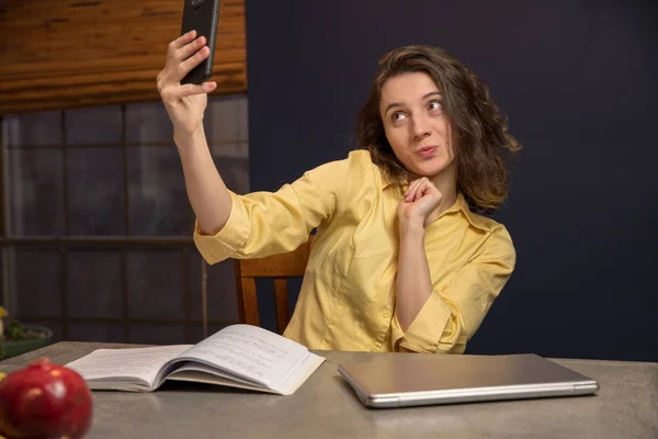 Giovane studentessa universitaria che lavora nella sua cucina scattando un selfie — Foto Stock