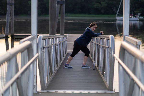 Older woman stretching in the early morning by a river — Stock Photo, Image