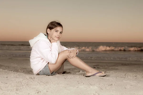 8-jähriges Mädchen sitzt in der Abenddämmerung am Strand — Stockfoto