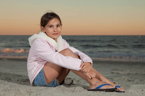 Niña de 8 años sentada en la playa al atardecer — Foto de Stock