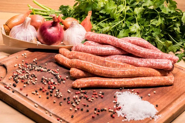 Raw sausages with chilli and herbs on a wooden board with spices — Stock Photo, Image