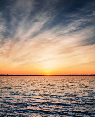 Alçak dramatik bulutlar üzerinde karanlık su üzerinde turuncu gün batımı